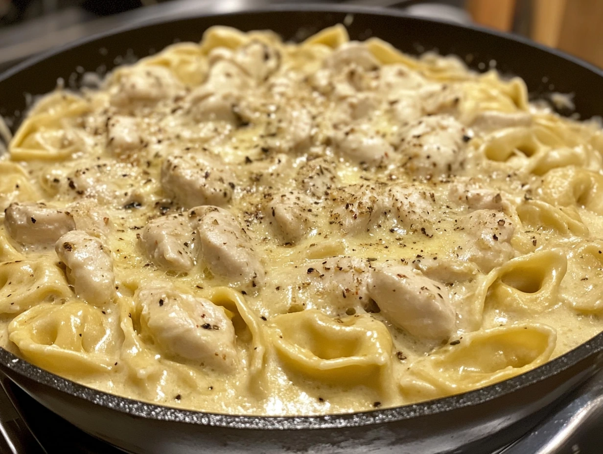A creamy bowl of cheese-filled tortellini and tender chicken pieces smothered in rich Alfredo sauce, garnished with fresh parsley.
