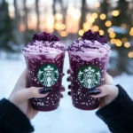 Purple Drink Frappuccino in a clear glass with whipped cream and blackberries on top.